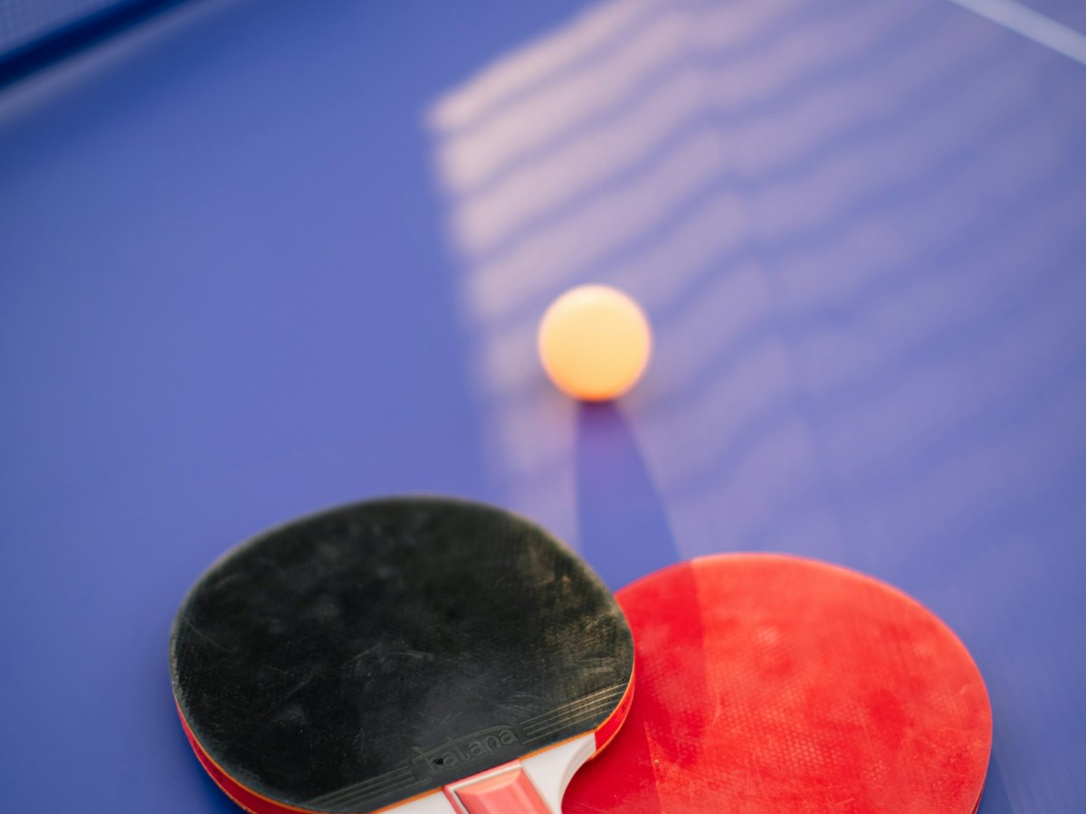 Table tennis paddles and ball on a blue table in warm light
